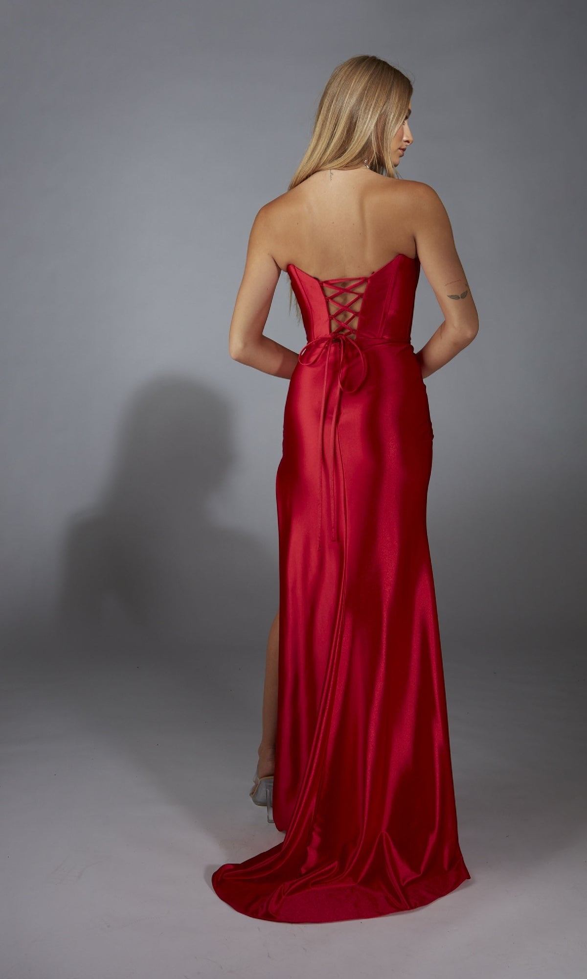 A woman with long blonde hair models the Strapless Corset Prom Dress: Aerie Couture 311, featuring a corset bodice and lace-up back, against a plain gray background.